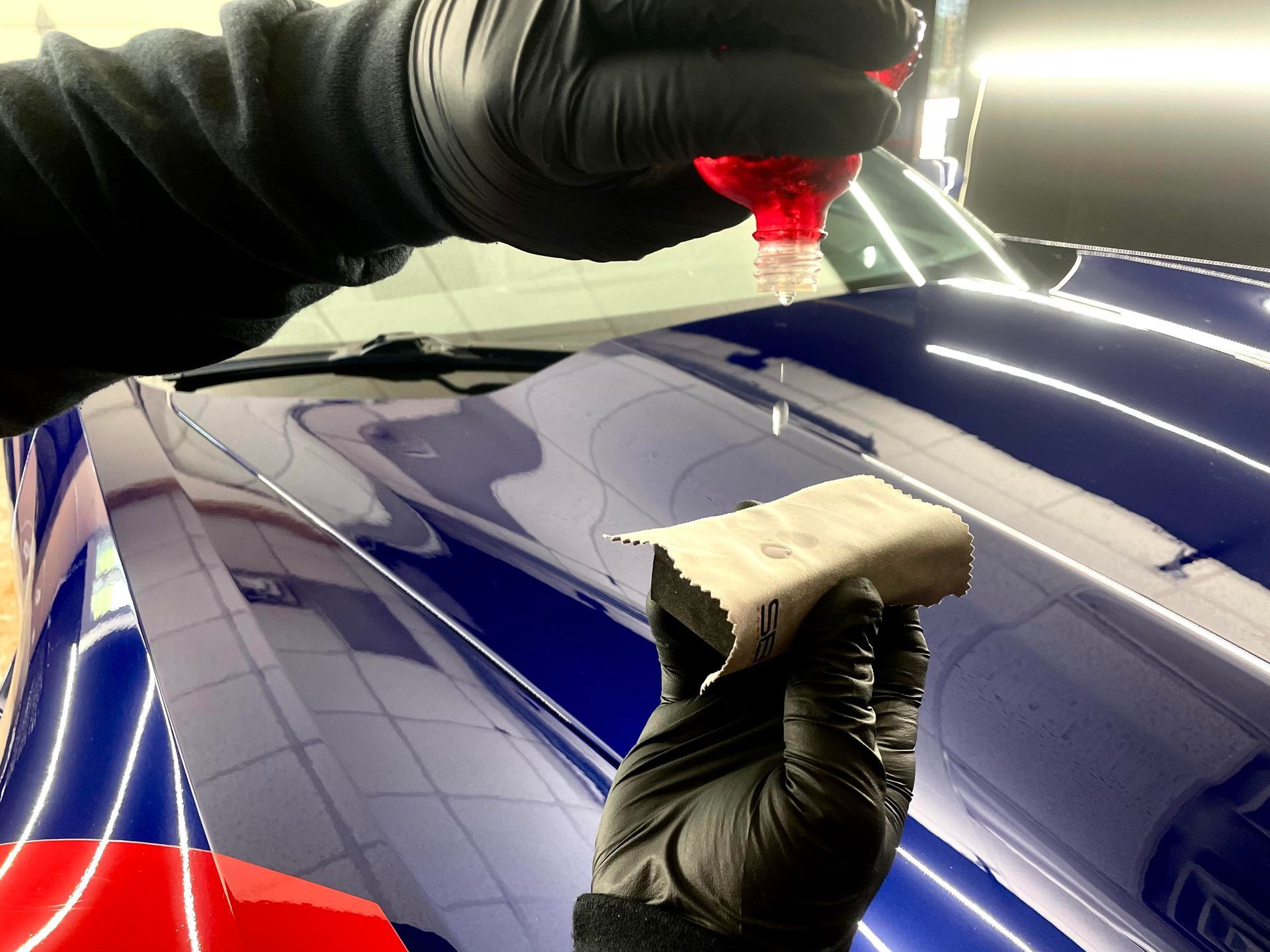 A person wearing black gloves is cleaning a blue car with a sponge.