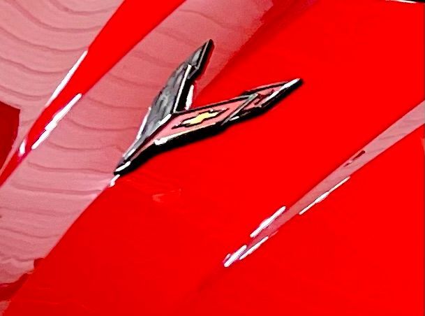 A black sports car is parked next to a red trailer in a parking lot.
