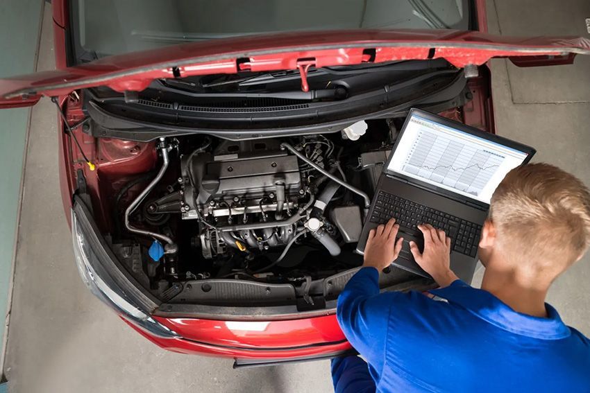 A Man is Working on the Engine of a Car While Using a Laptop Computer — Toowoomba Lube & Mechanical in Glenvale, QLD