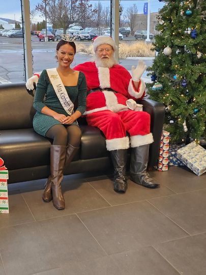 Woman and Santa seated on a couch beside a decorated Christmas tree in a lobby