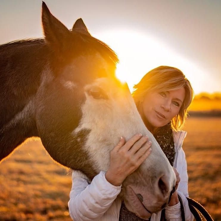 Woman gently hugs a black-and-white horse at sunset in a field