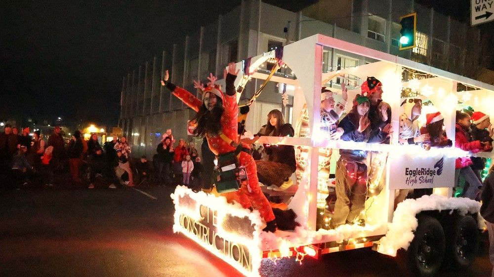 Decorated holiday parade float with people in costumes and bright lights at night