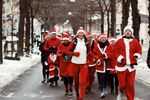Group dressed in red and white Santa outfits walking on a snowy street during a winter parade