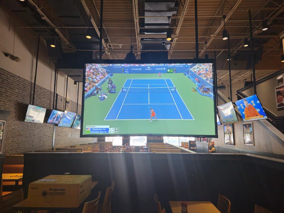Indoor sports bar with a large TV showing a blue tennis match and smaller screens around it