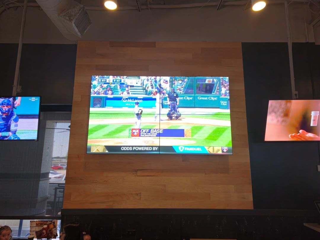 Sports broadcast on a large wall-mounted screen in a dim indoor venue, with smaller side screens visible.