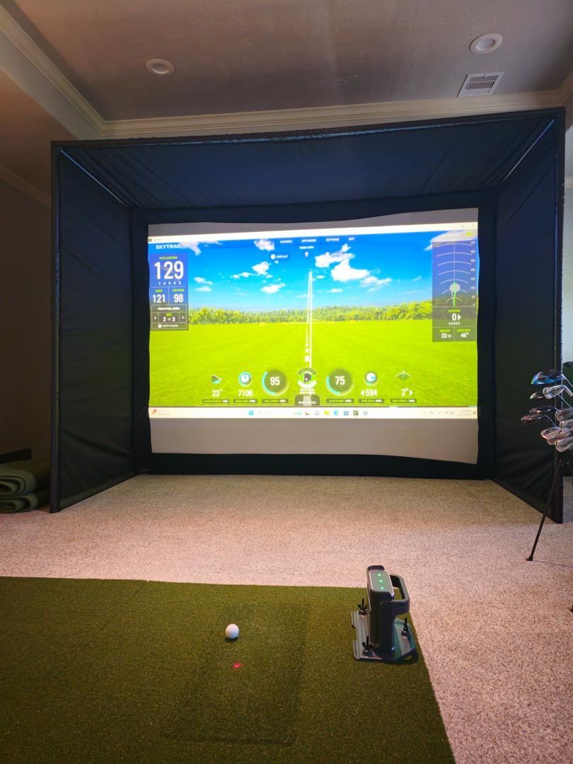 Indoor golf simulator with a projected driving range, ball on the mat, and club stand in the foreground