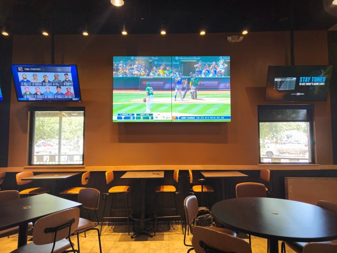 Restaurant lounge with multiple TVs showing a sports game above empty tables and chairs
