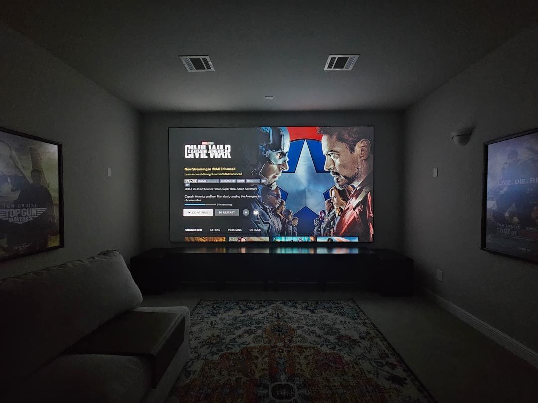 Dark home theater with a projected video game menu on the front wall and two side screens showing cars.