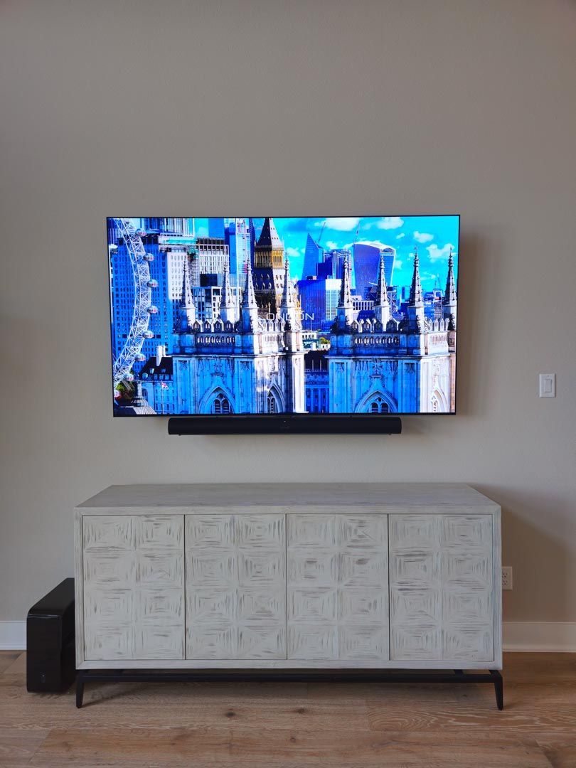 Wall-mounted TV displaying a blue cityscape above a white console in a minimalist room