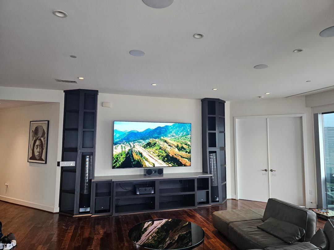 Modern living room with wall-mounted TV, built-in shelving, dark wood floor, and a gray sectional sofa