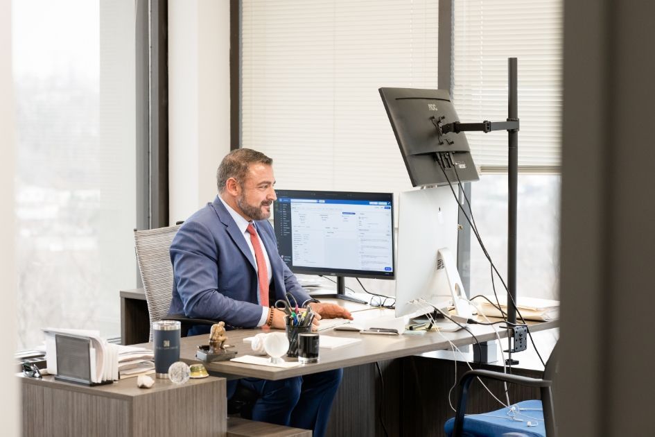 A man in a suit and tie is sitting at a desk in front of a computer.