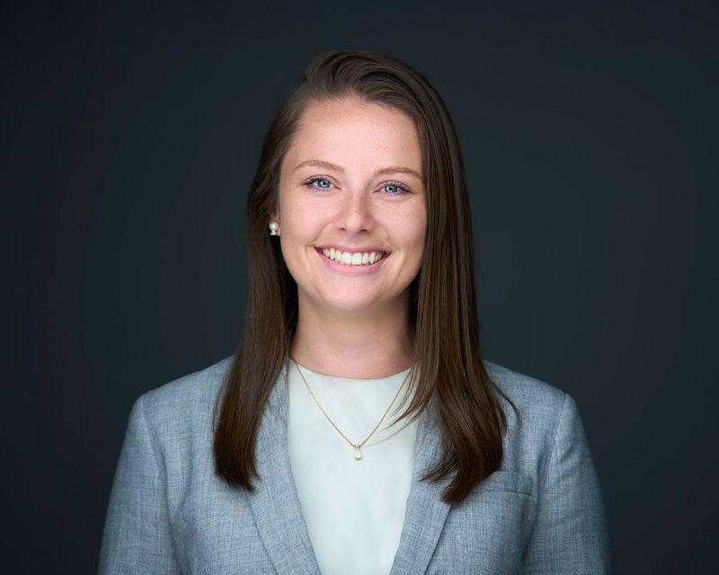 A woman in a suit and necklace is smiling for the camera.