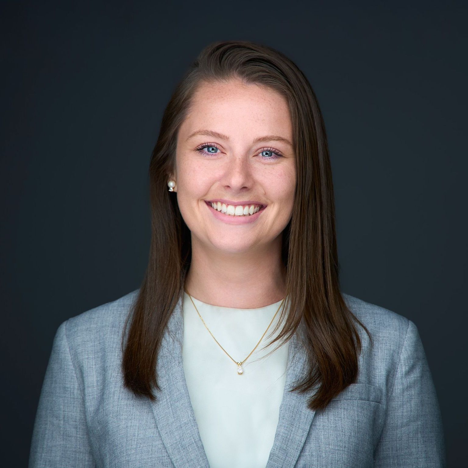 A woman in a grey jacket and white shirt is smiling for the camera.