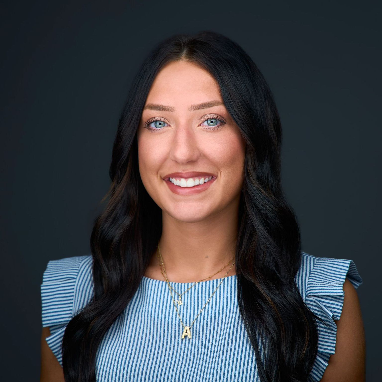 A woman wearing a blue striped shirt and a necklace is smiling for the camera.