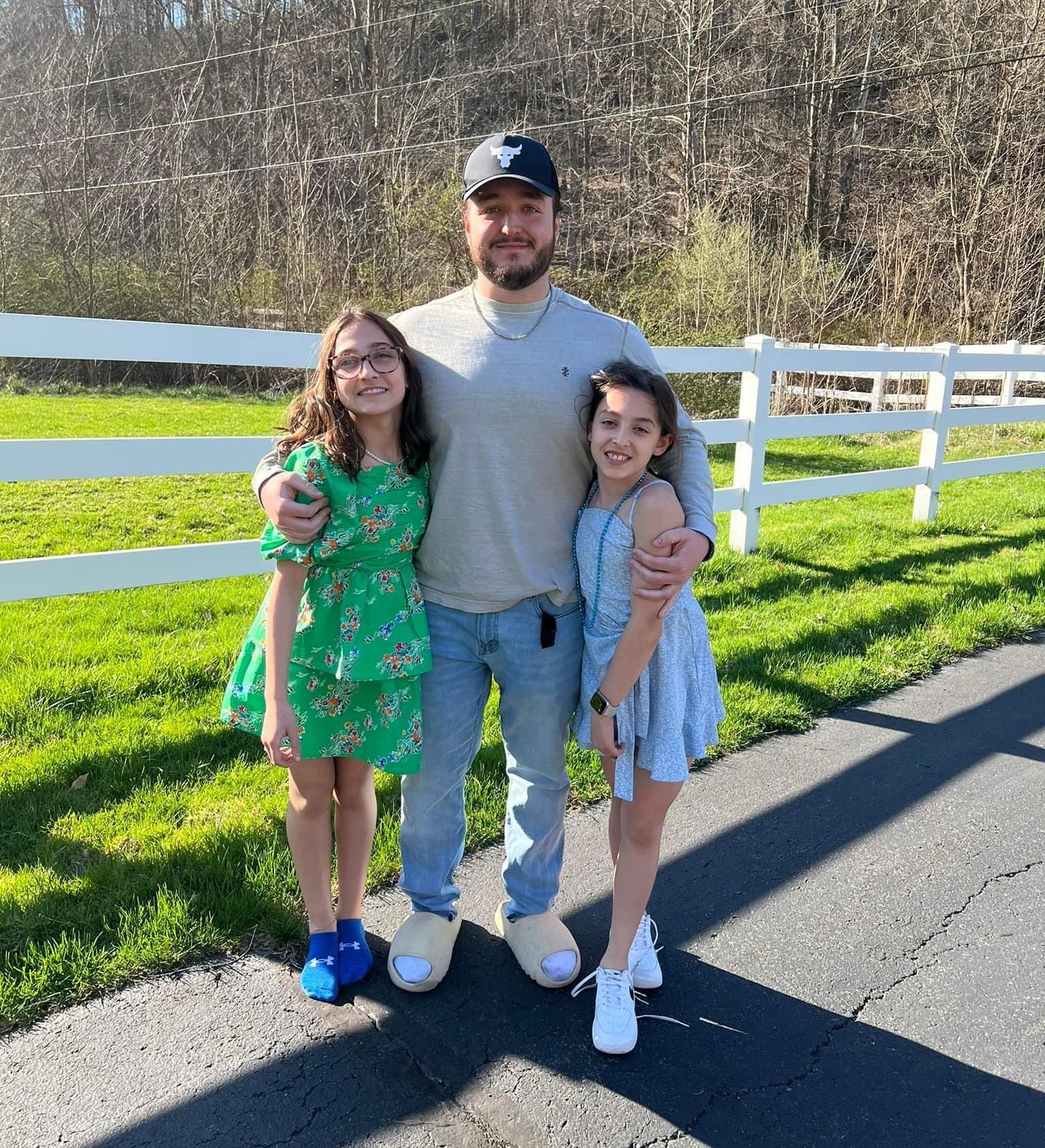 A man and two girls are posing for a picture in front of a white fence.