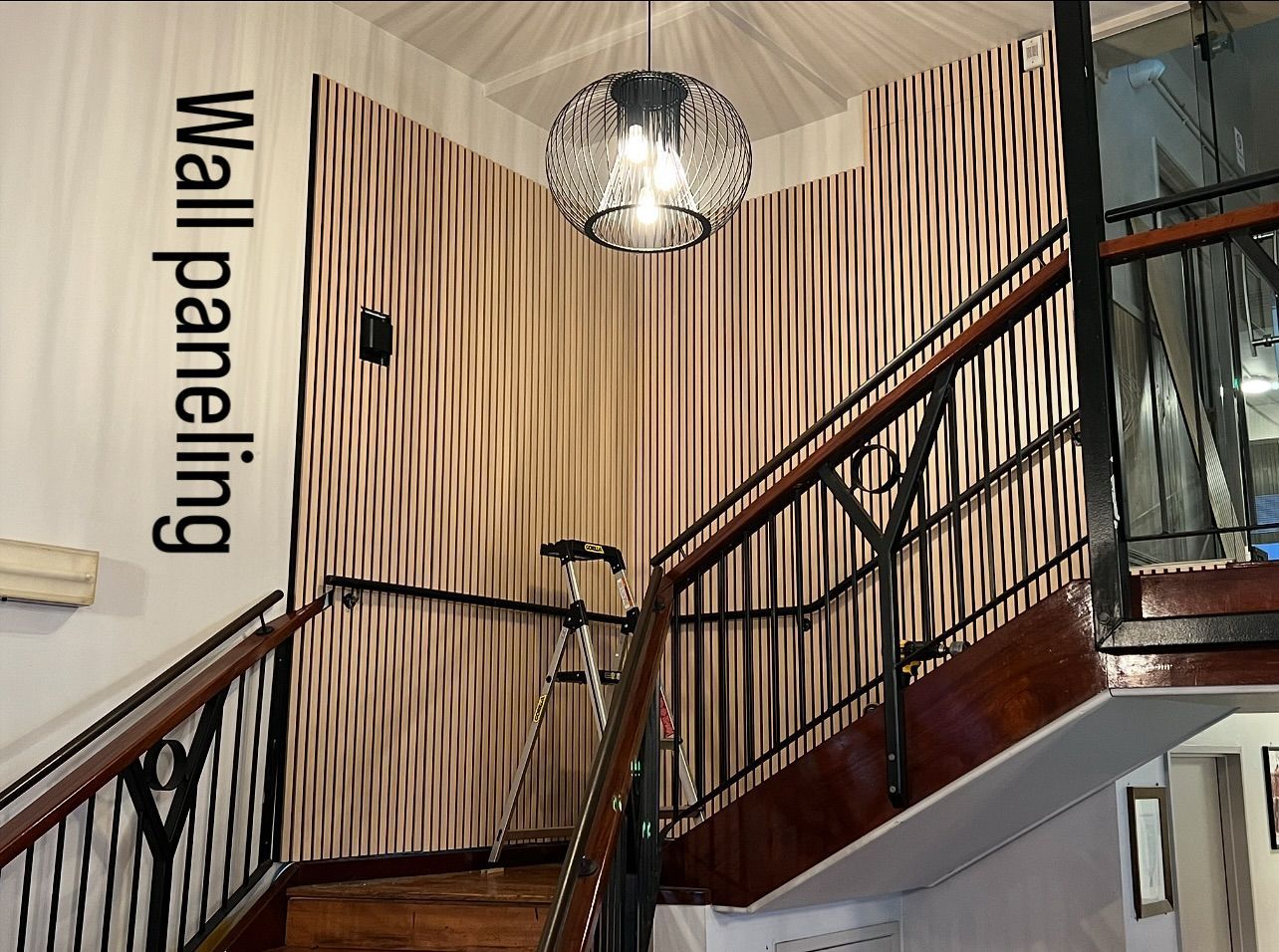 Staircase with brown and tan patterned wall paneling, black railing, and a hanging light fixture.