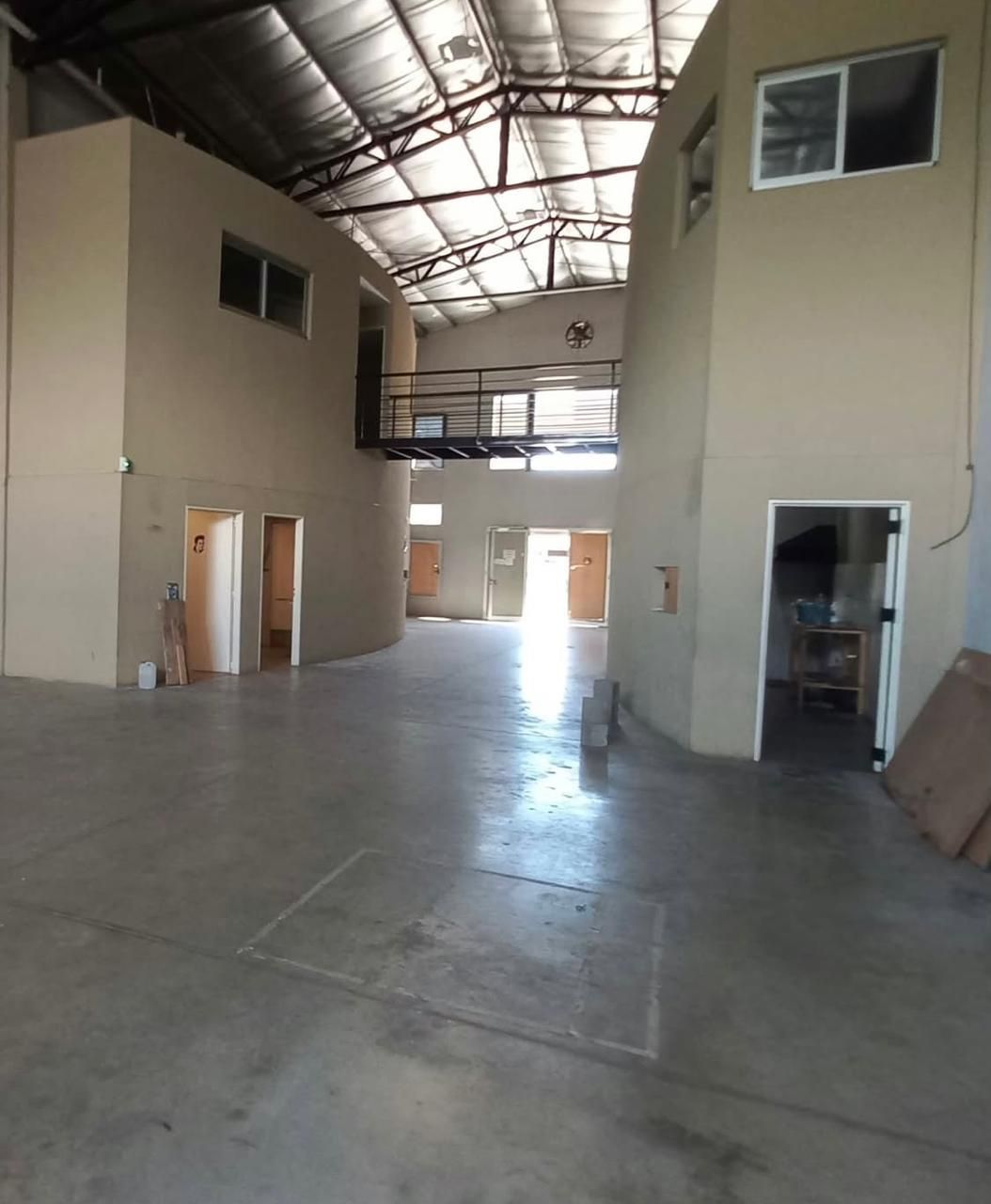 Interior de un almacén vacío con suelo de hormigón, paredes beige y techo metálico alto.