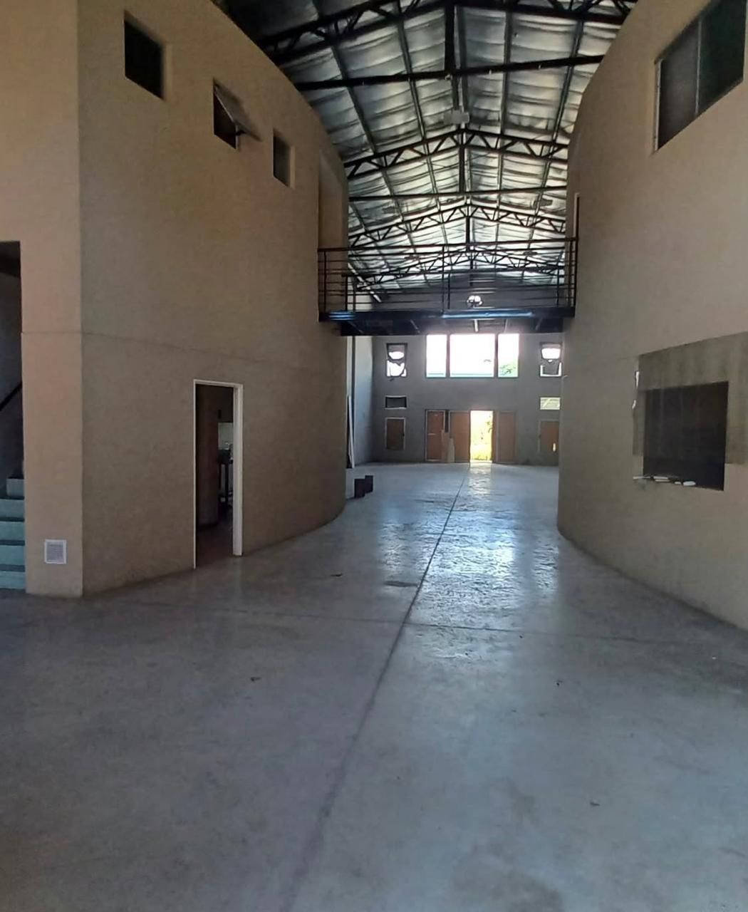 Pasillo de almacén vacío con techo alto de metal, suelo de hormigón y puertas a lo largo de los laterales.