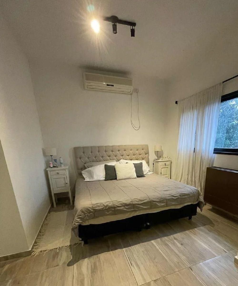 Dormitorio con cama, mesitas de noche, aire acondicionado y ventana.