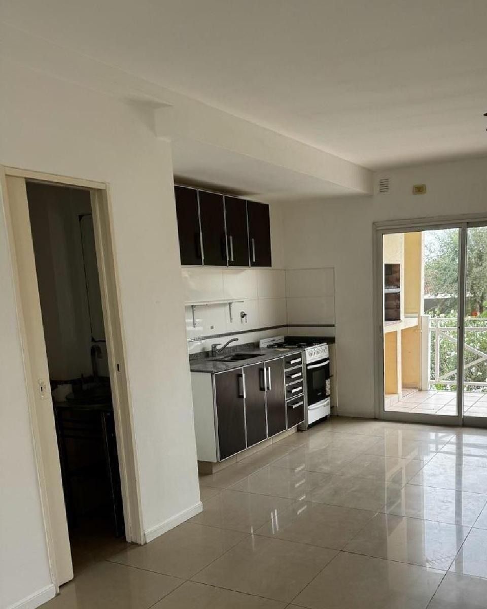 Cocina moderna y vacía con armarios oscuros, suelo de baldosas y puertas correderas de cristal que dan a un balcón.