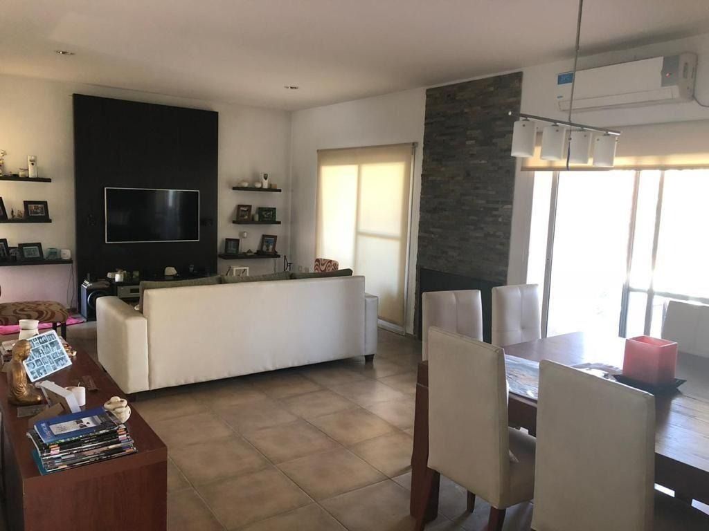 Salón con sofá blanco, televisor, mesa de comedor y pared decorativa de piedra.