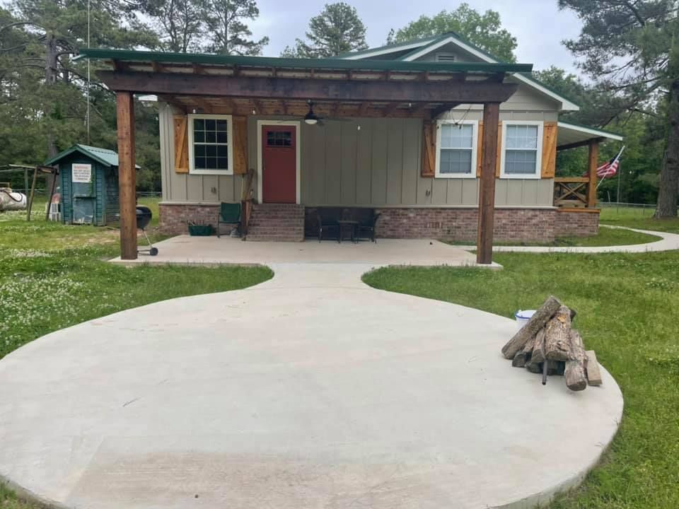 Small house with covered porch and circular concrete driveway, with a fire pit in the foreground.