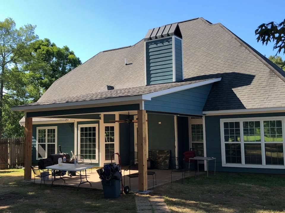 Backyard house with covered patio, white trim, and a large dormer under a sunny blue sky