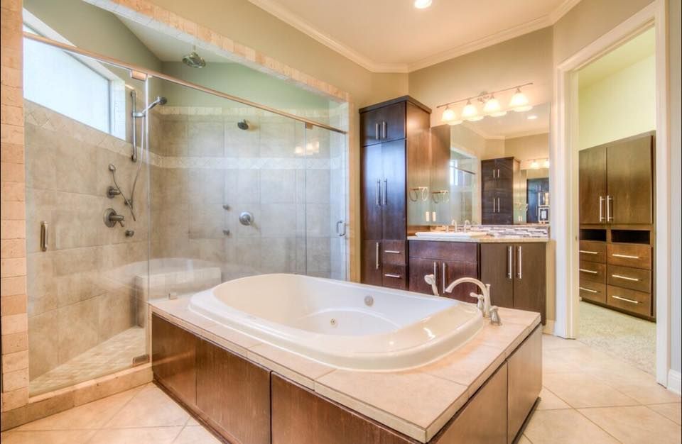 Spacious beige bathroom with a corner soaking tub, glass shower, double vanity, and large mirror lights