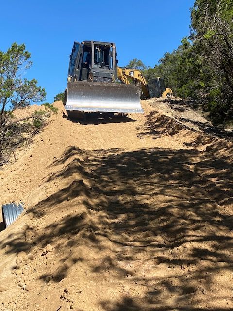 Bulldozer blade scraping a sandy hillside under a blue sky.