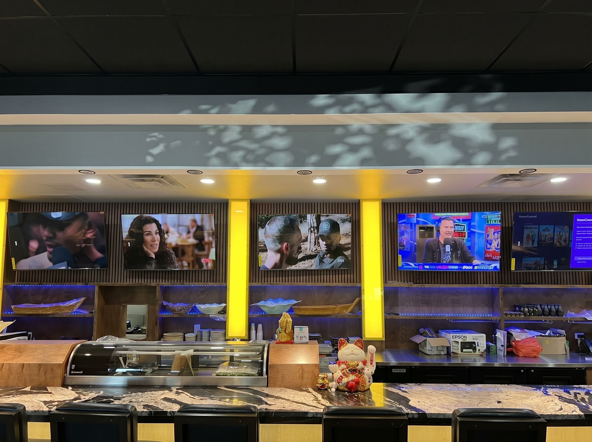 Buffet counter with food trays and illuminated TV screens above in a restaurant or sports bar