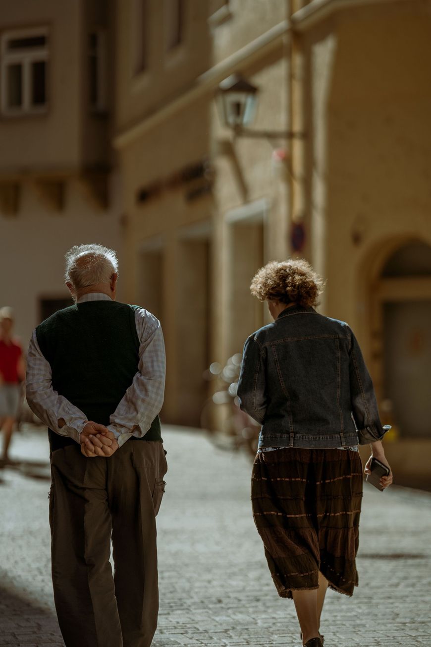 Two people walking away down a cobblestone street in a sunlit village.