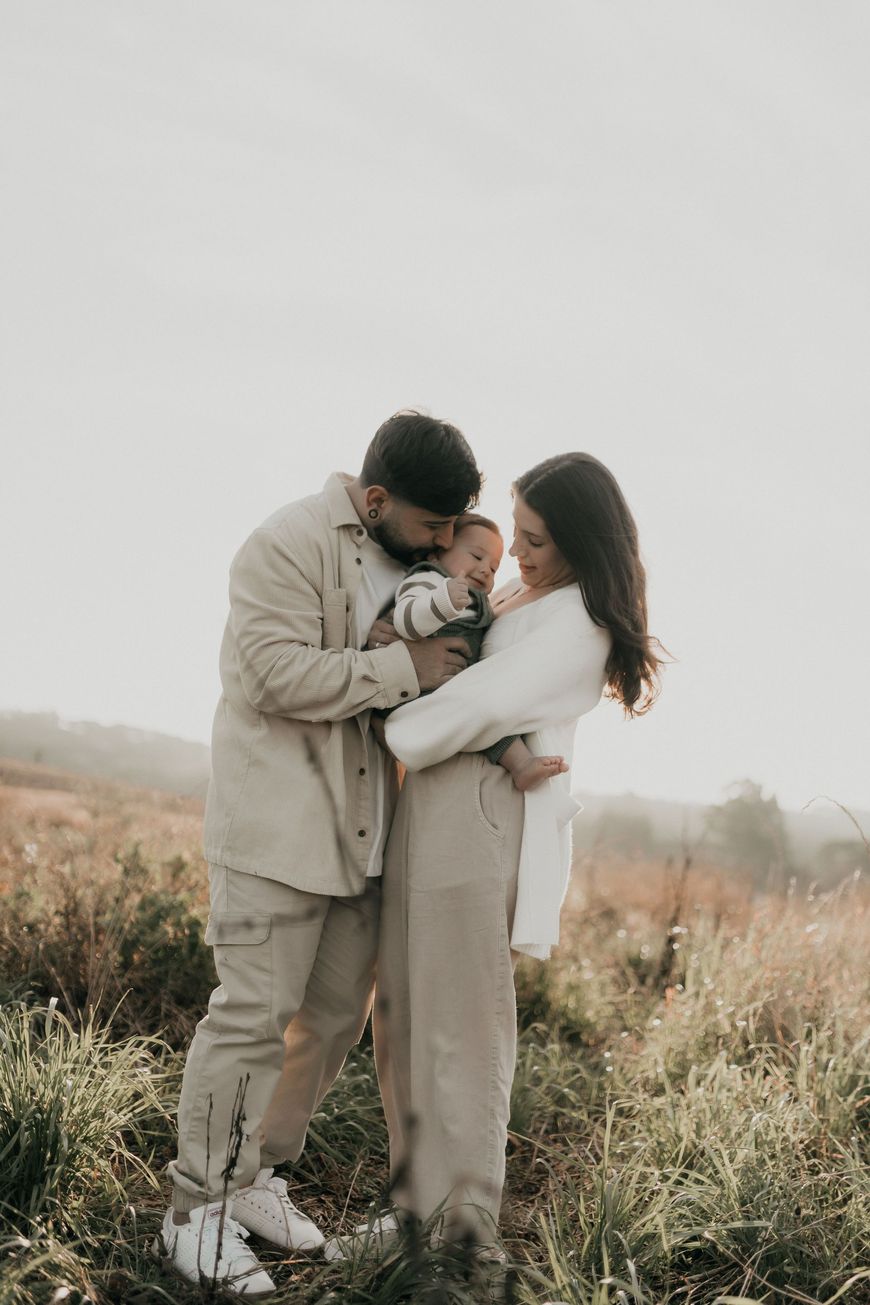 Couple embracing in a grassy field, both in light beige outfits under a soft gray sky