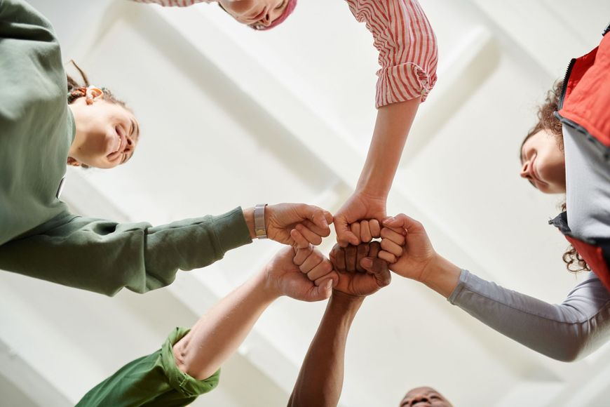 Several people stack hands in a circle, showing teamwork and unity indoors.