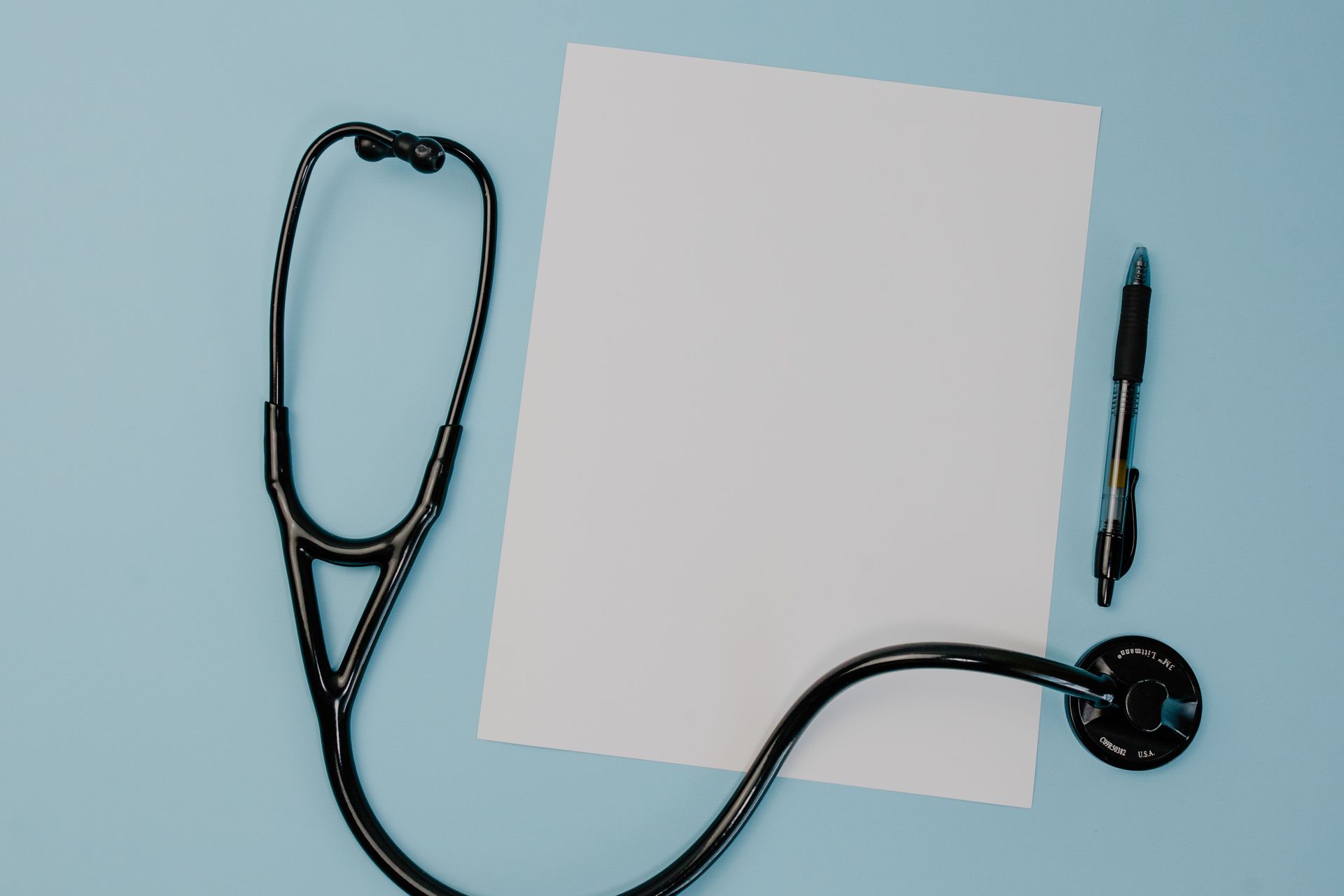 Stethoscope, blank white paper, and pen on a light blue background
