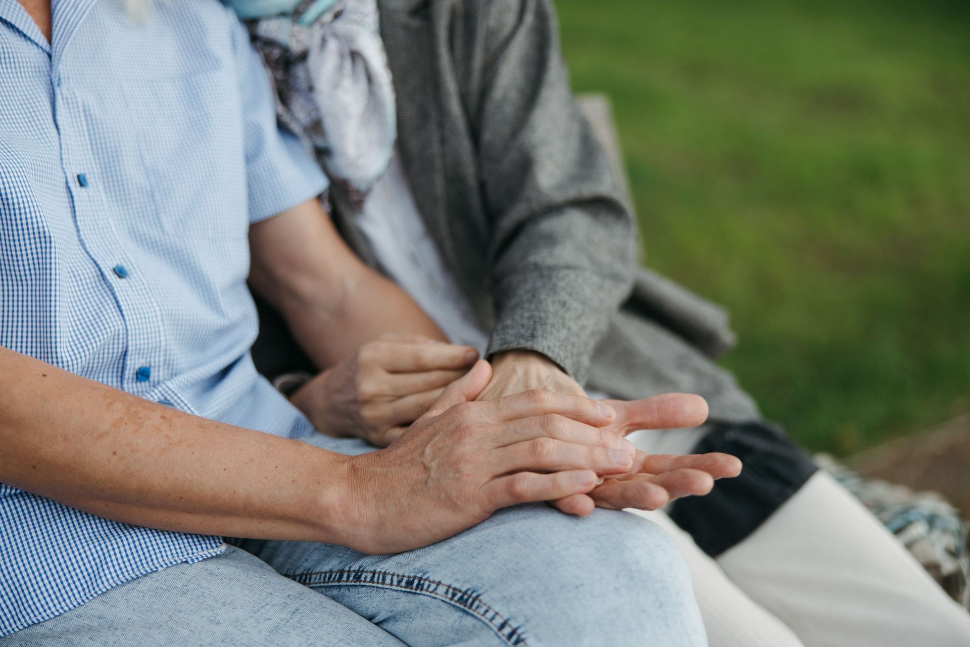 Two people seated outdoors, holding hands on a bench