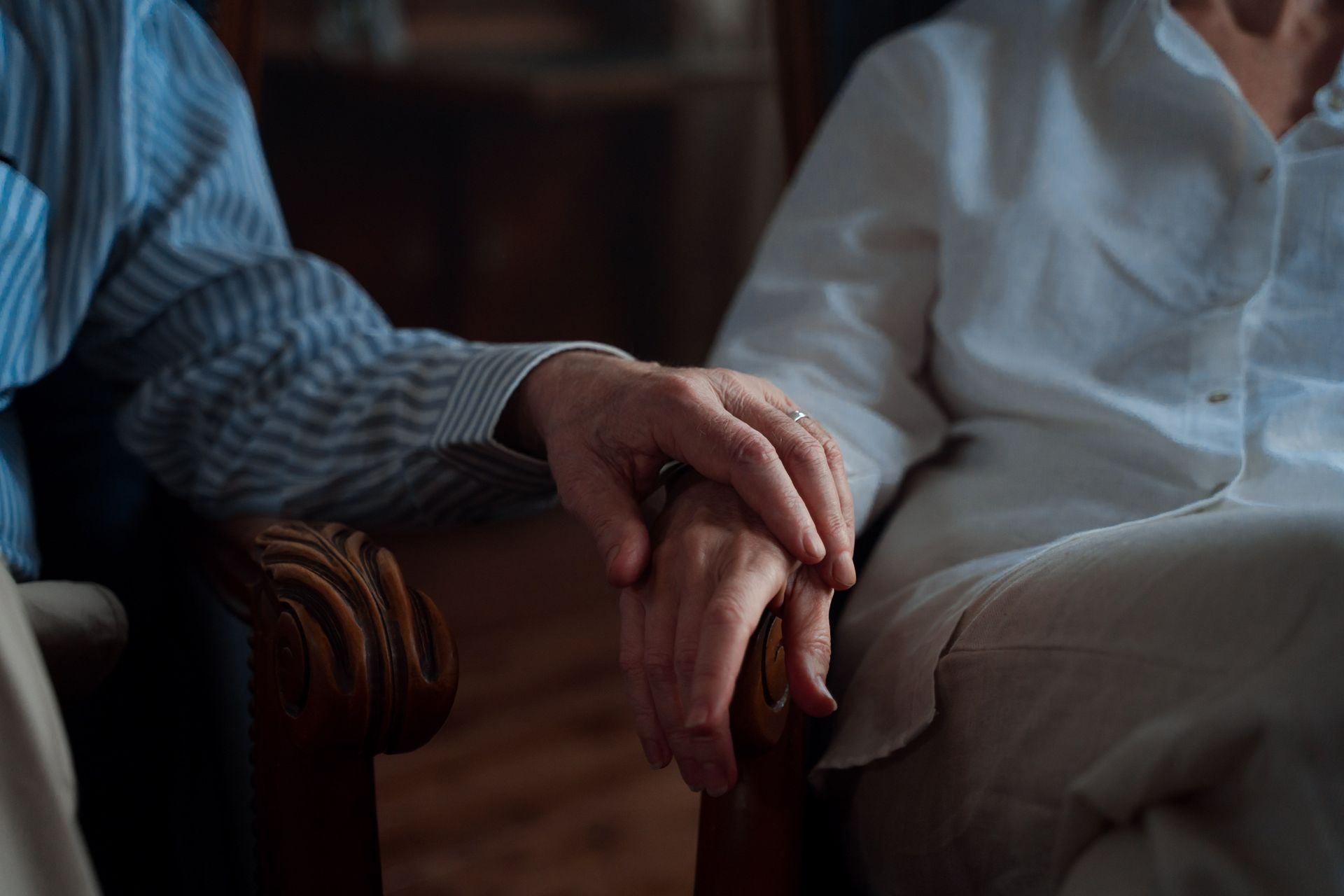 Two people sitting close together, one hand gently resting on the other’s hand in a dim room