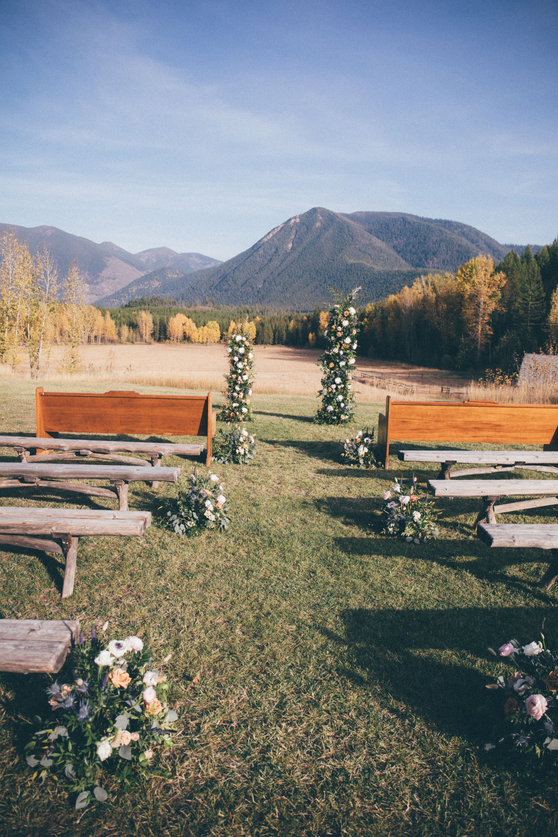 A row of wooden benches in a field with mountains in the background.