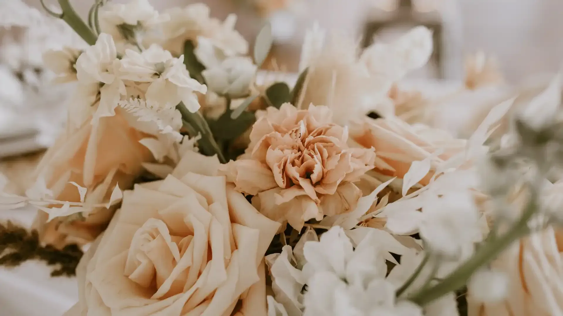 Close-up of a bouquet with peach, cream, and white flowers, including roses and carnations.