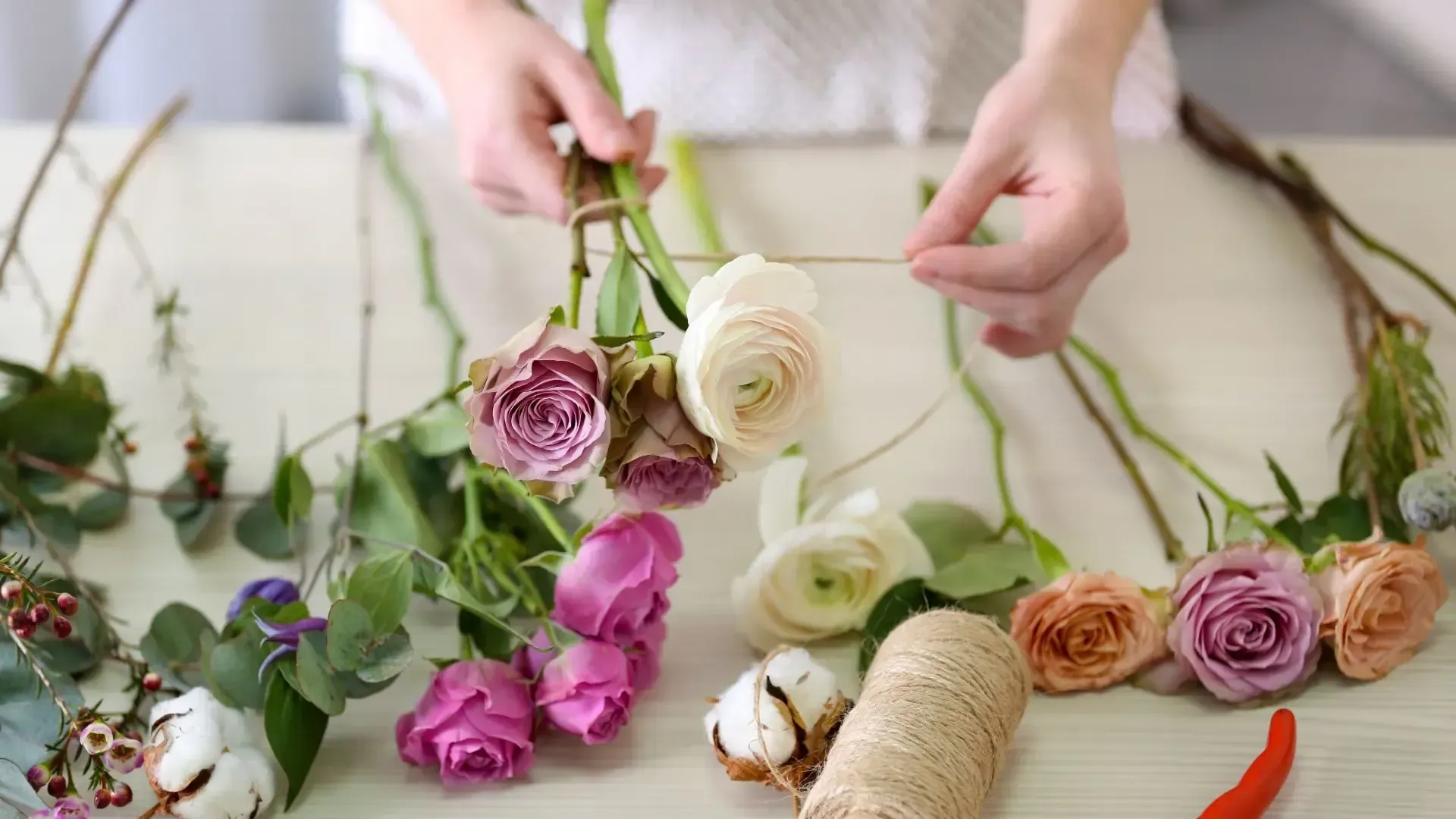 A person is making a wreath of flowers on a table.
