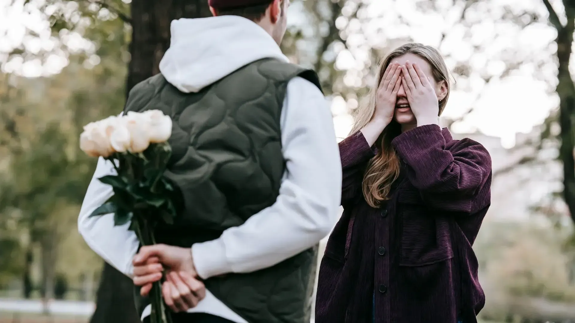 A man is hiding a bouquet of flowers behind his back for a woman.