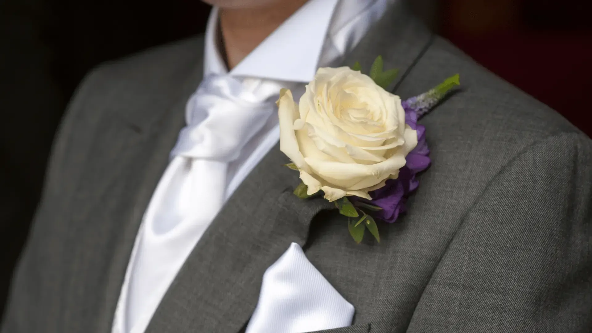A man in a suit has a white rose on his jacket.