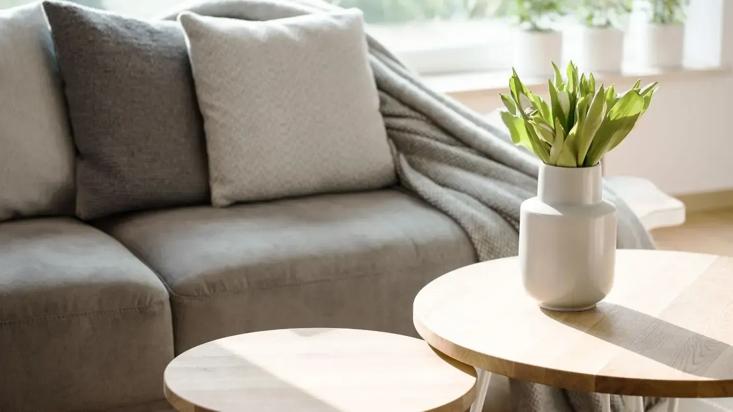 Living room with gray sofa and pillows, wooden tables, vase of tulips.