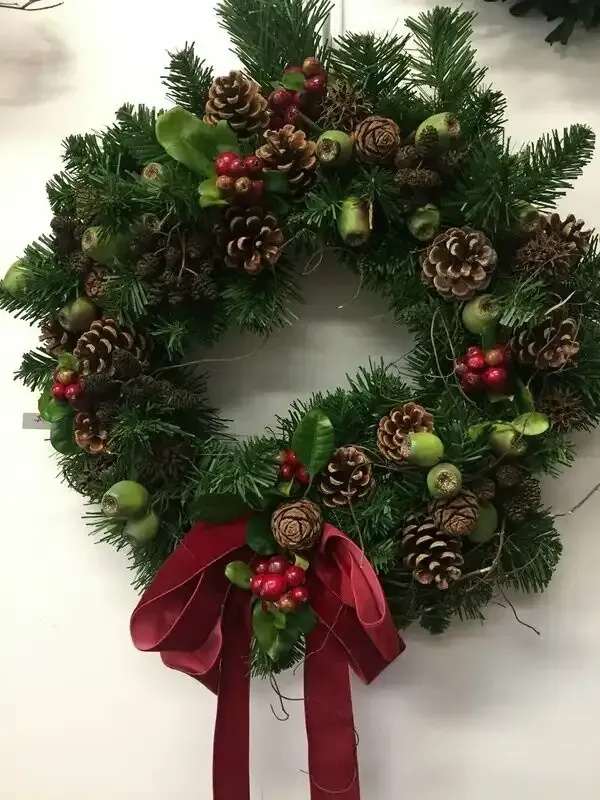 a christmas wreath with pine cones berries and a red bow