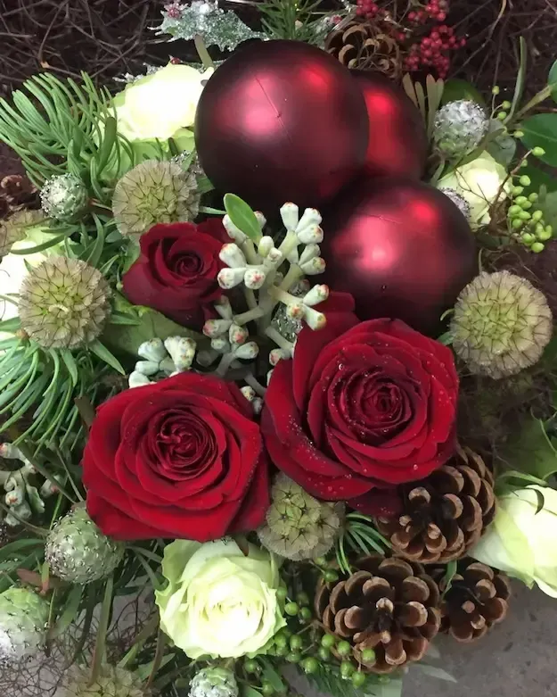 A bouquet of red roses , pine cones , and christmas balls