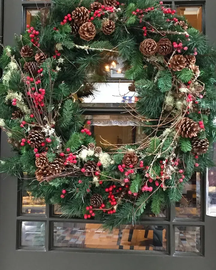 A christmas wreath is hanging on a glass door.