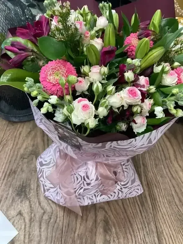 A bouquet of flowers wrapped in pink paper is sitting on a wooden table.