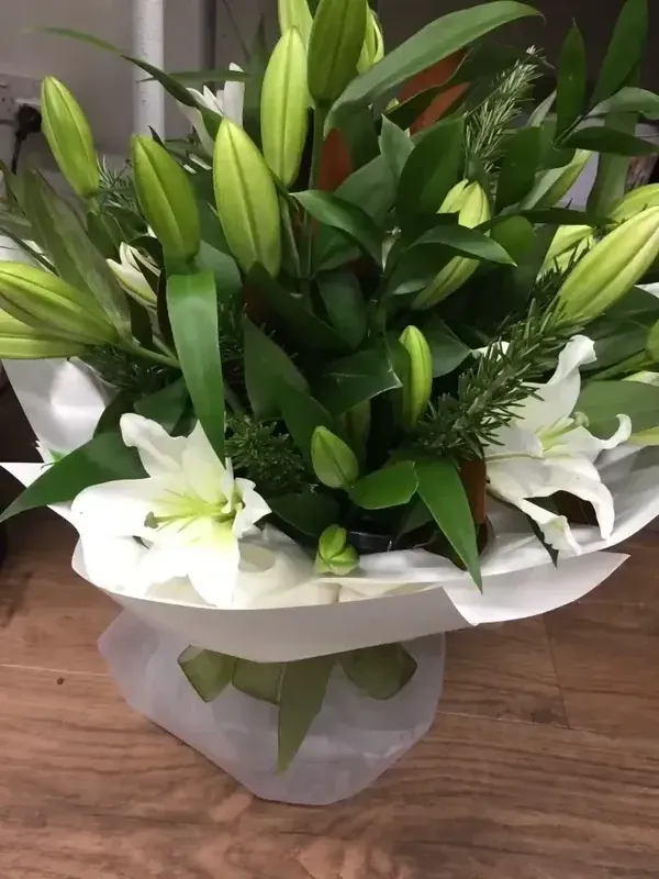 A vase filled with white flowers and green leaves on a wooden table.