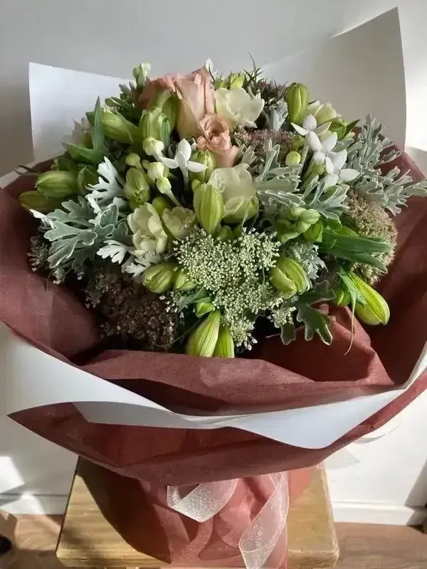 Something Special Posy in a Vox Box A bouquet of flowers wrapped in red and white paper is sitting on a wooden table.