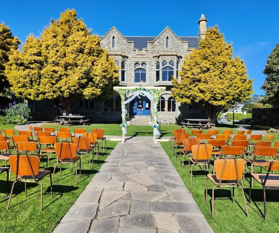 Wedding ceremony setup outdoors with chairs, arch, stone path, and building.