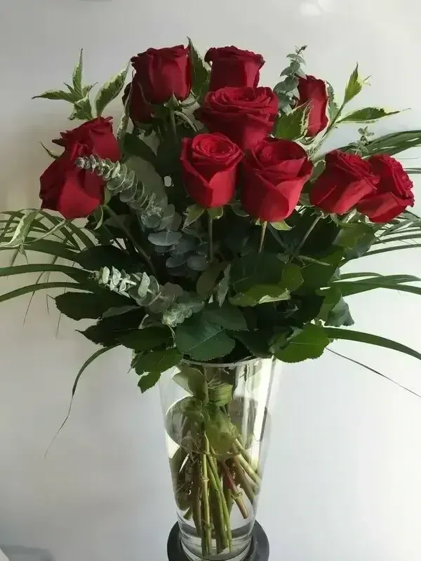 A clear glass vase filled with a bouquet of vibrant red roses and green eucalyptus foliage against a white background.